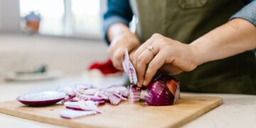 Close-up of a woman chopping fresh red onion in a kitchen setting.