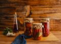 Jars of preserved vegetables on a wooden surface with a rustic background.