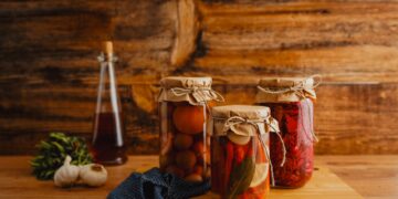 Jars of preserved vegetables on a wooden surface with a rustic background.