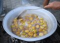 Large outdoor pot boiling yellow plums. Traditional cooking process with hand stirring.