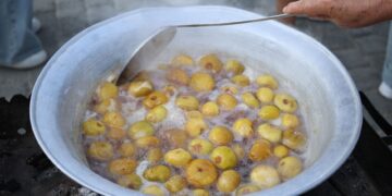 Large outdoor pot boiling yellow plums. Traditional cooking process with hand stirring.