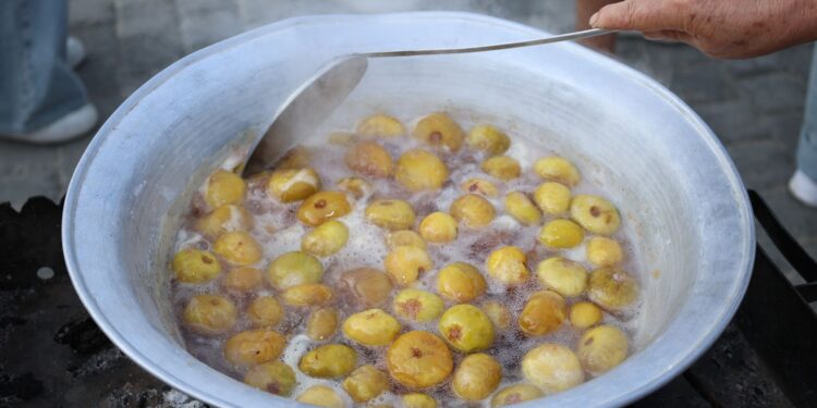 Large outdoor pot boiling yellow plums. Traditional cooking process with hand stirring.