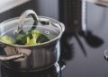 Close-up of broccoli steaming in a stainless steel pot on a modern stovetop indoors.