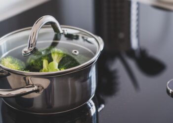 Close-up of broccoli steaming in a stainless steel pot on a modern stovetop indoors.