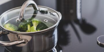 Close-up of broccoli steaming in a stainless steel pot on a modern stovetop indoors.