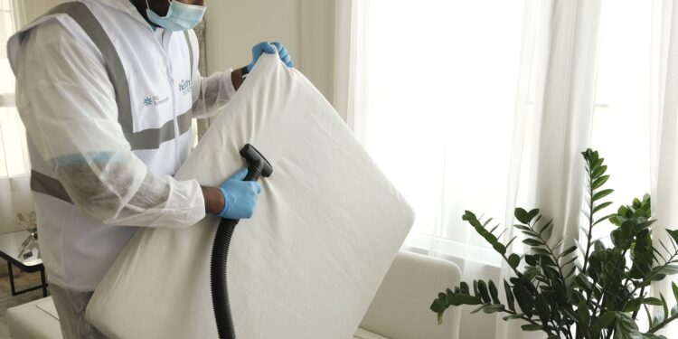 Man in protective gear vacuuming a mattress in a modern home interior.