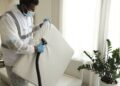 Man in protective gear vacuuming a mattress in a modern home interior.