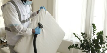 Man in protective gear vacuuming a mattress in a modern home interior.