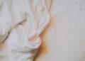 An artistic close-up of crumpled white bed sheets in soft, warm lighting.