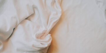An artistic close-up of crumpled white bed sheets in soft, warm lighting.