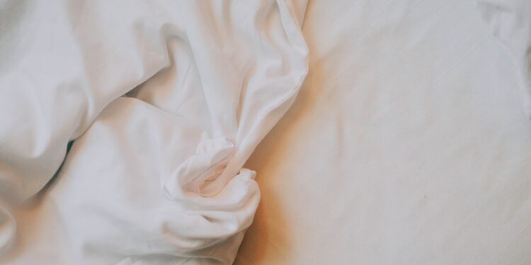 An artistic close-up of crumpled white bed sheets in soft, warm lighting.