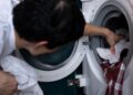 Close-up of a man placing clothes into a washing machine during household chores.