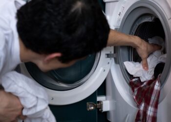 Close-up of a man placing clothes into a washing machine during household chores.
