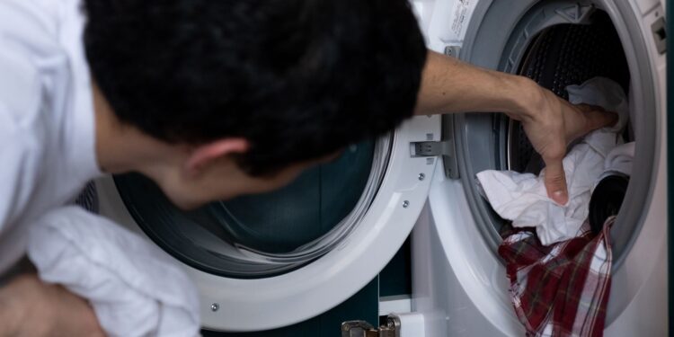 Close-up of a man placing clothes into a washing machine during household chores.