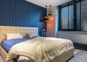 Modern bedroom interior with blanket and pillows on bed against lamps and jalousie in house