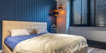 Modern bedroom interior with blanket and pillows on bed against lamps and jalousie in house