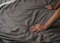Close-up of hands smoothing gray wrinkled bed linen fabric, highlighting texture and softness.