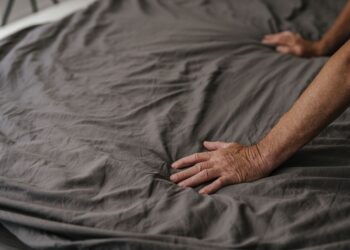 Close-up of hands smoothing gray wrinkled bed linen fabric, highlighting texture and softness.