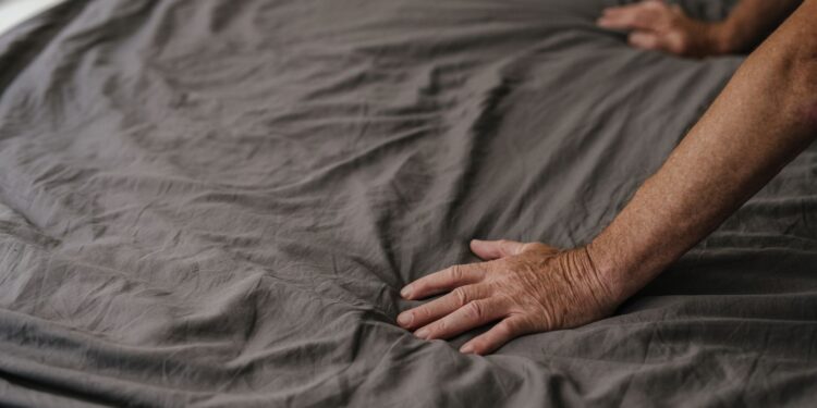 Close-up of hands smoothing gray wrinkled bed linen fabric, highlighting texture and softness.