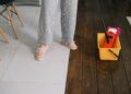 Crop anonymous woman in gumshoes and pants dipping mop into bucket with water on parquet in house