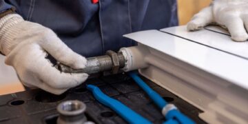 Close-up of a plumber installing a radiator pipe using specialized tools.