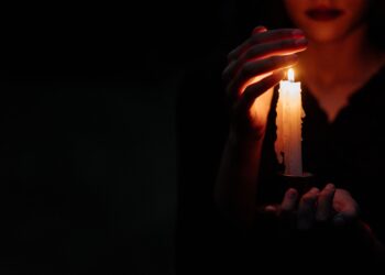 Close-up of a person in the dark holding a single lit candle, creating a moody atmosphere.