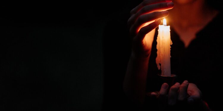 Close-up of a person in the dark holding a single lit candle, creating a moody atmosphere.