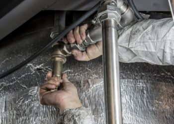 Close-up of a plumber's hands installing steel pipes indoors, showcasing skilled manual work.
