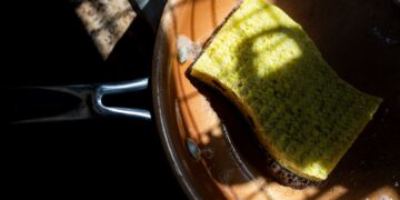 A yellow sponge rests in a copper pan, lit by dramatic shadows. Ideal for cleaning themes.