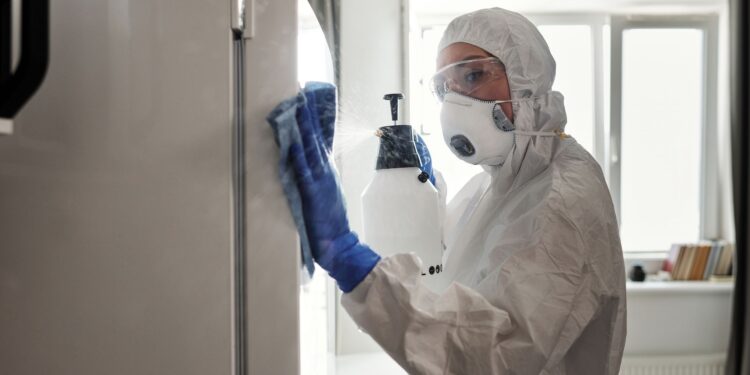 Person in protective gear sanitizing refrigerator at home for safety.