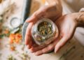 Close-up of hands holding a glass jar filled with colorful dried herbs.
