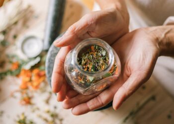 Close-up of hands holding a glass jar filled with colorful dried herbs.