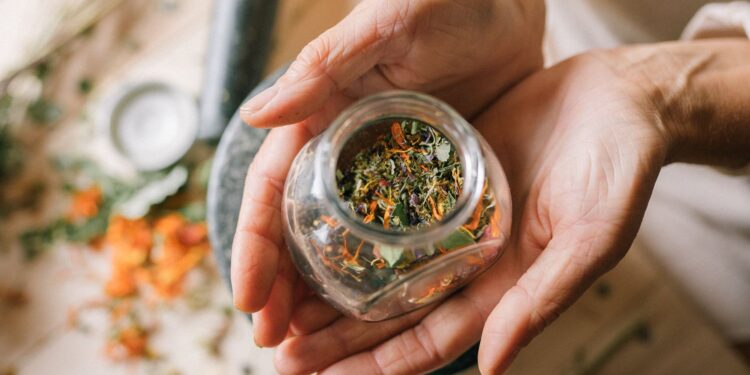 Close-up of hands holding a glass jar filled with colorful dried herbs.