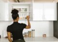 A woman organizing a pantry shelf with various food jars in a modern kitchen.
