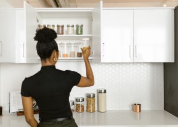 A woman organizing a pantry shelf with various food jars in a modern kitchen.