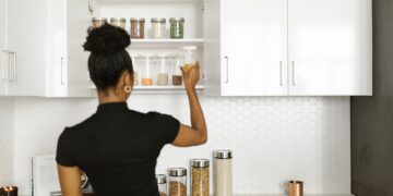 A woman organizing a pantry shelf with various food jars in a modern kitchen.