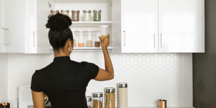 A woman organizing a pantry shelf with various food jars in a modern kitchen.
