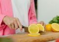 A close-up photo of hands slicing a lemon on a wooden chopping board, perfect for culinary or kitchen themes.