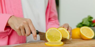 A close-up photo of hands slicing a lemon on a wooden chopping board, perfect for culinary or kitchen themes.