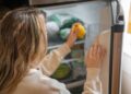 Woman reaching for a lemon in the fridge, illustrating healthy living habits.