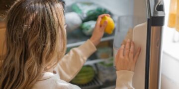 Woman reaching for a lemon in the fridge, illustrating healthy living habits.