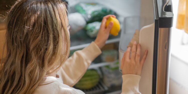 Woman reaching for a lemon in the fridge, illustrating healthy living habits.