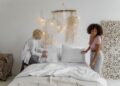 Side view of multiracial young same sex couple setting bed in cozy bedroom in morning