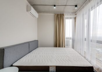 Spacious modern bedroom with a clean mattress and large windows for natural light.