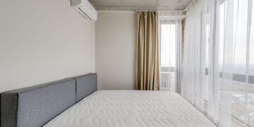 Spacious modern bedroom with a clean mattress and large windows for natural light.