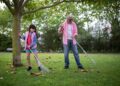 Warm family moment outdoors with grandfather and granddaughter raking leaves in a park.