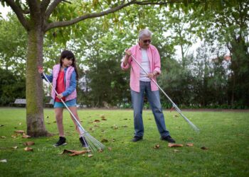 Warm family moment outdoors with grandfather and granddaughter raking leaves in a park.