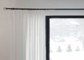White curtains partially covering a window with a snowy outdoor view. Minimalist home decor.