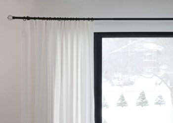 White curtains partially covering a window with a snowy outdoor view. Minimalist home decor.
