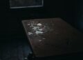 A moody shot of broken glass pieces scattered on an old wooden table in a dimly lit room.